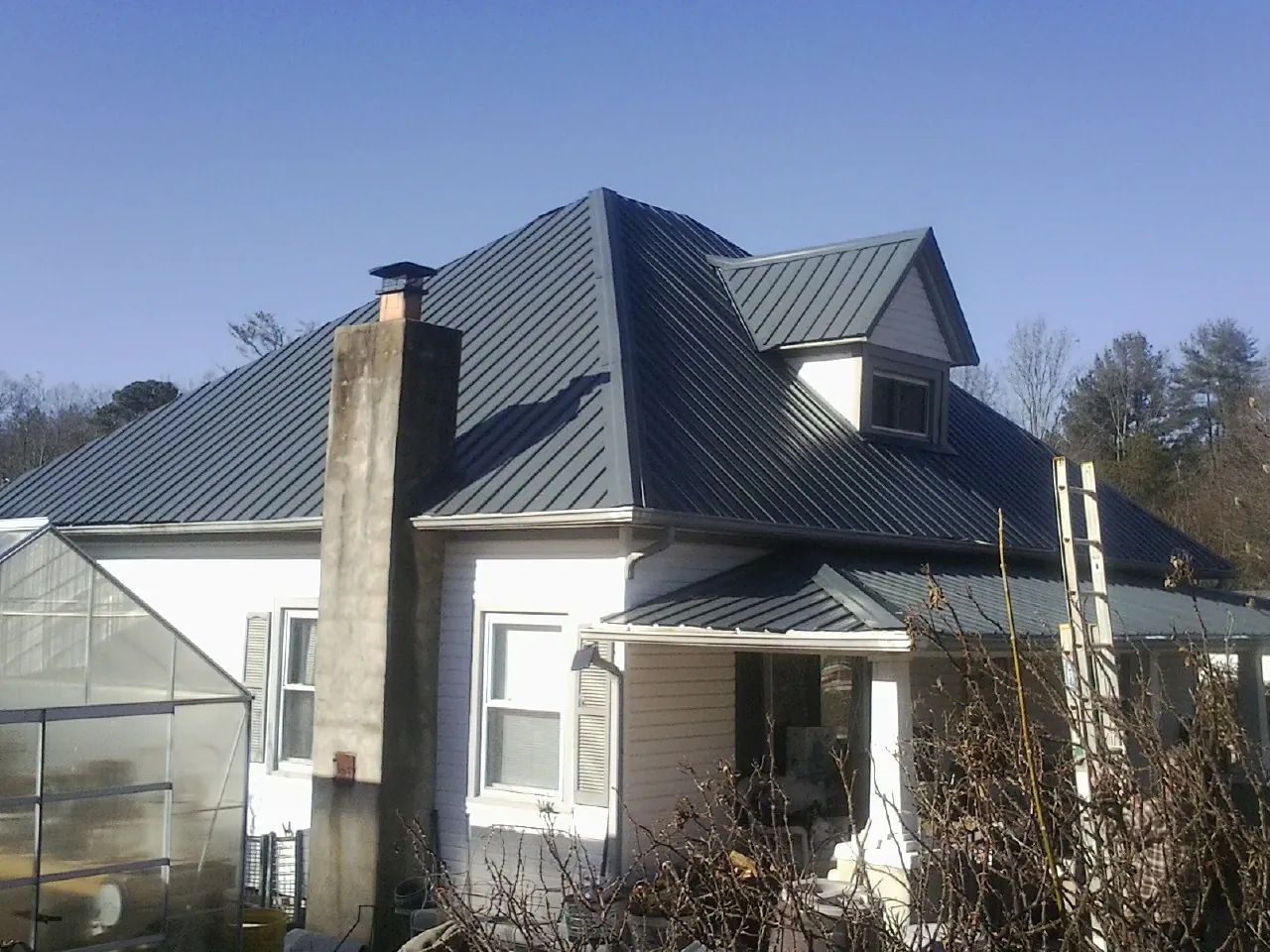 Dark blue standing seam metal roof on a white farmhouse with dormer — Slate & Tile Roof Repair by Roofing Brothers in Armbrust