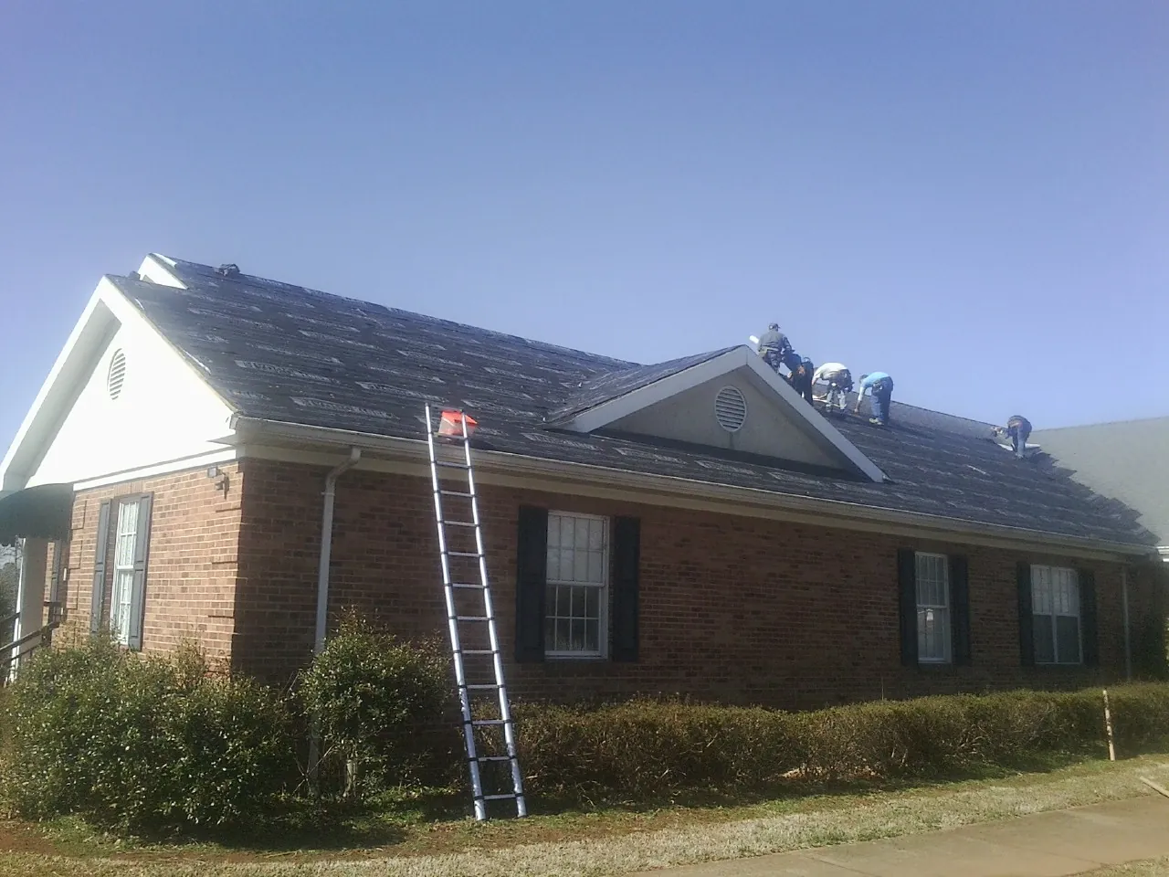 Crew tearing shingles off a brick ranch roof with a ladder set — Emergency Roof Repair work by our crew in Armbrust