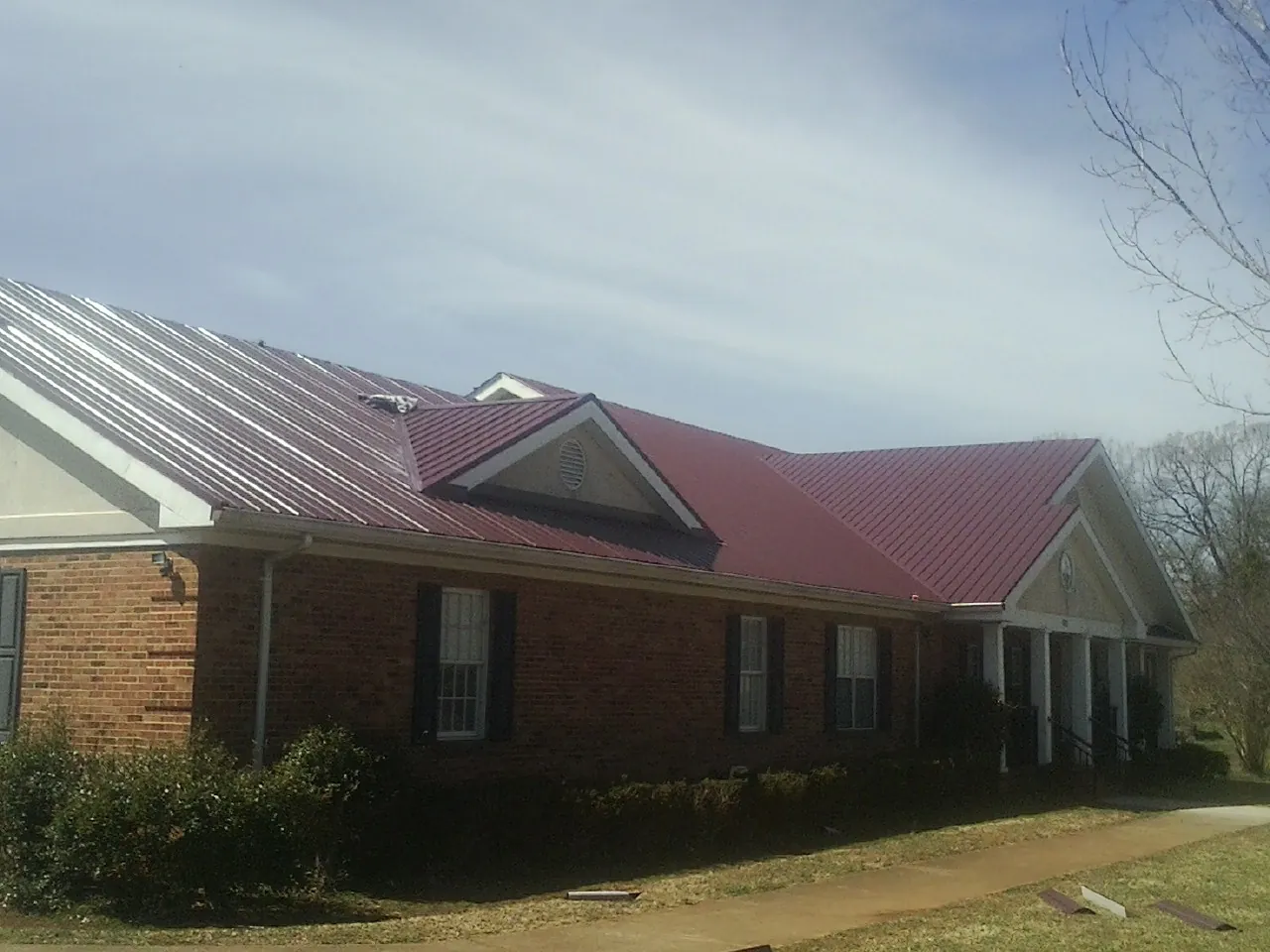 Red metal roof with gabled entries on a long brick building, from a Hail Damage Roof Repair job in Armbrust