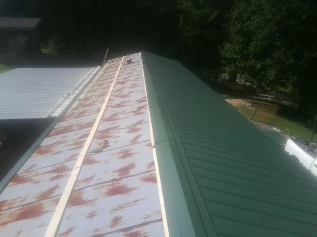 Old rusted panels beside newly installed green metal roofing — Wind Damage Roof Repair by Roofing Brothers in Armbrust