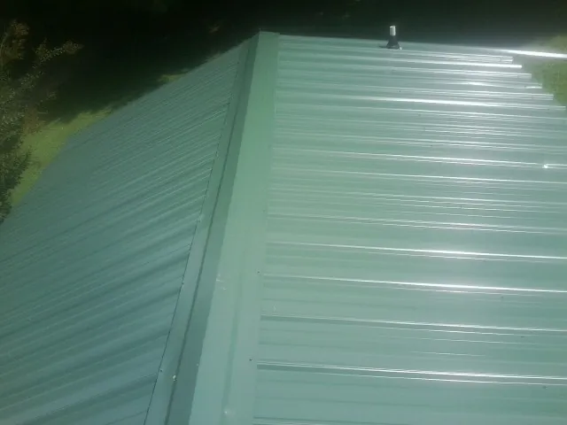 New green metal panels meeting at the ridge of a roof — Flat Roof Repair work by our crew in Armbrust