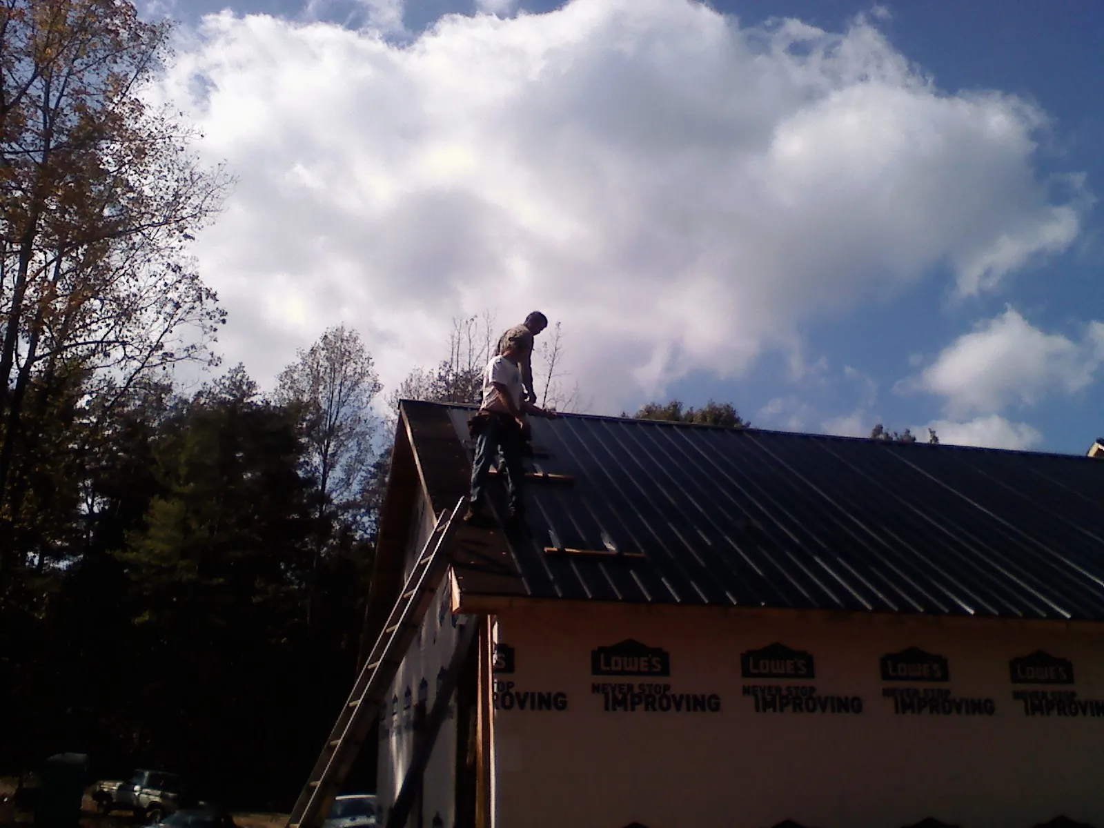 Roofer fastening dark metal panels high against a cloudy sky, from a Roof Inspection job in Armbrust