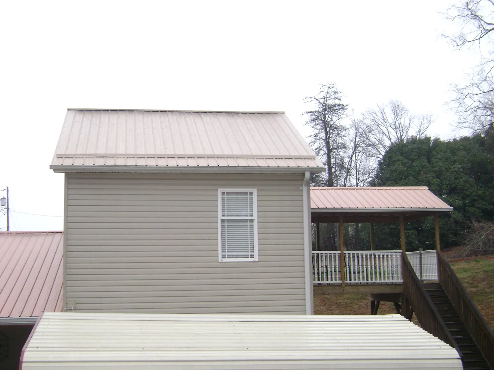 Tan metal roofs on a two story addition and attached porch, from a Roof Replacement job in Armbrust